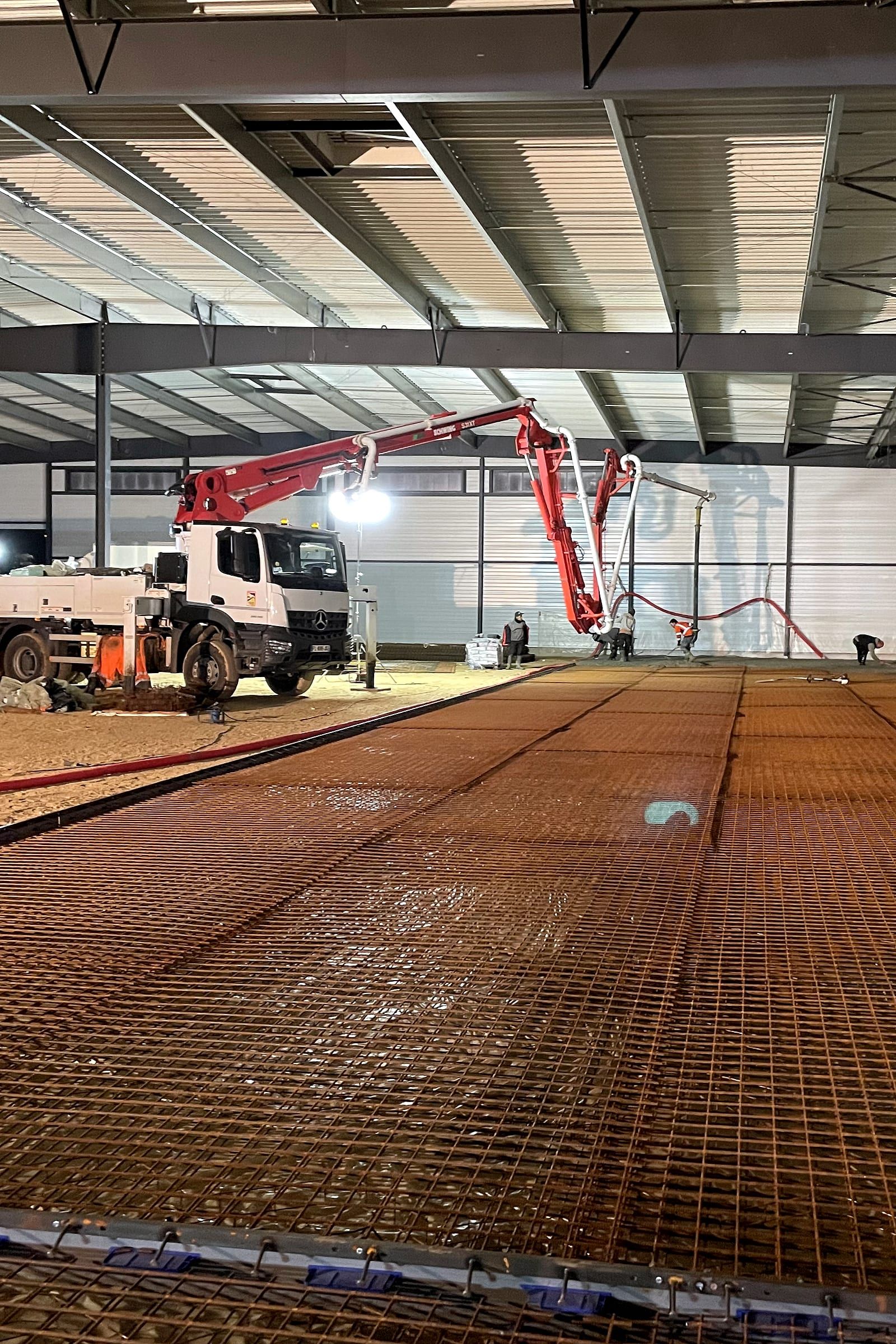 Camion-pompe déployé dans une halle, au bord de la nappe de treillis à couler